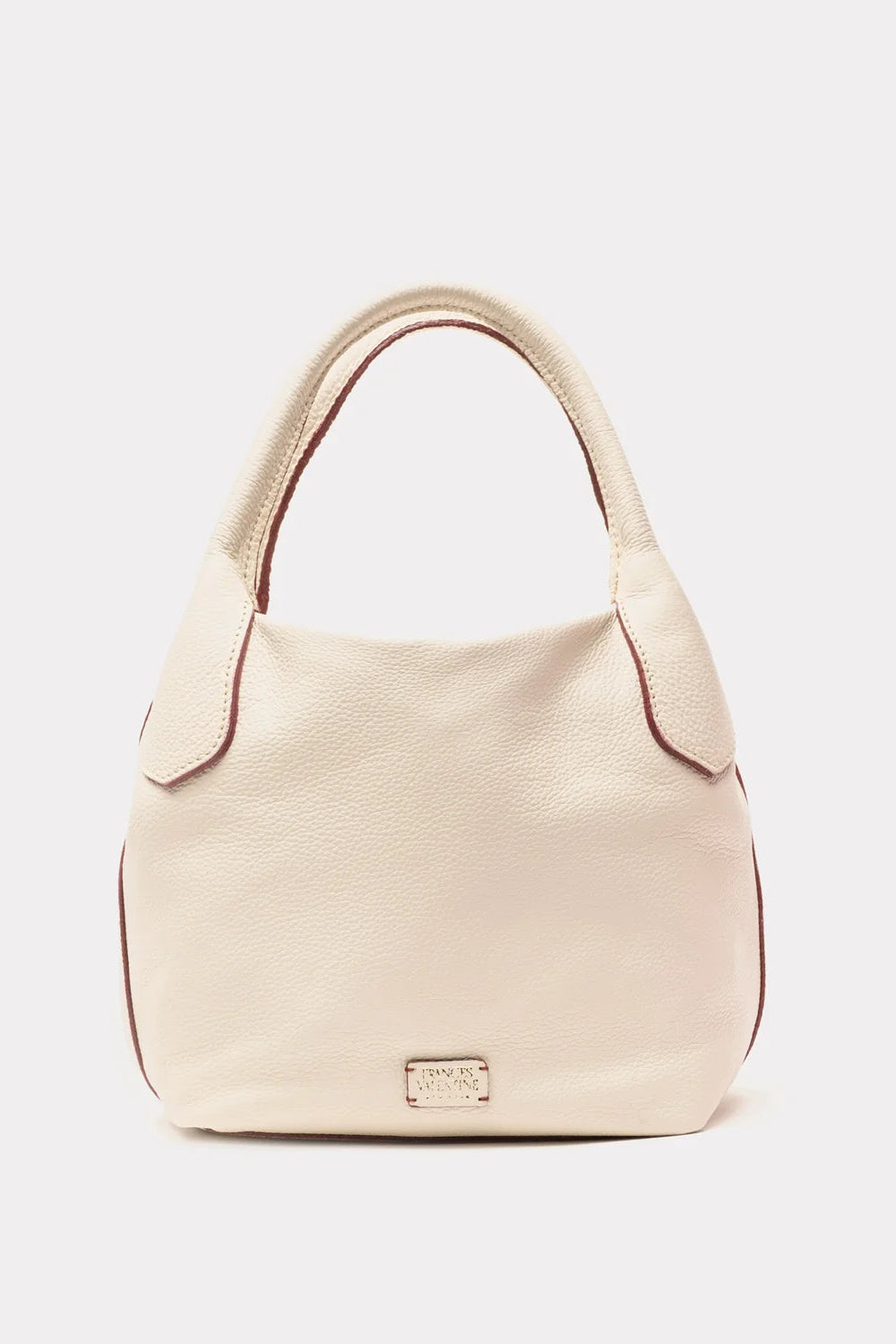 A light beige pebbled leather hobo handbag with contrasting dark red-brown piping and a small gold-tone metal logo plaque on the front, shown against a plain light gray background.