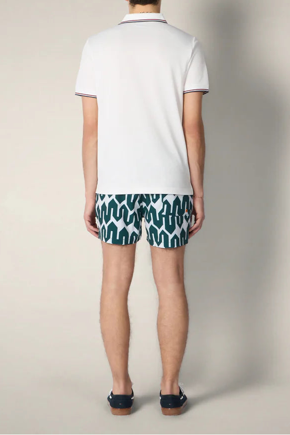 Person wearing a white polo shirt and patterned shorts on a plain background