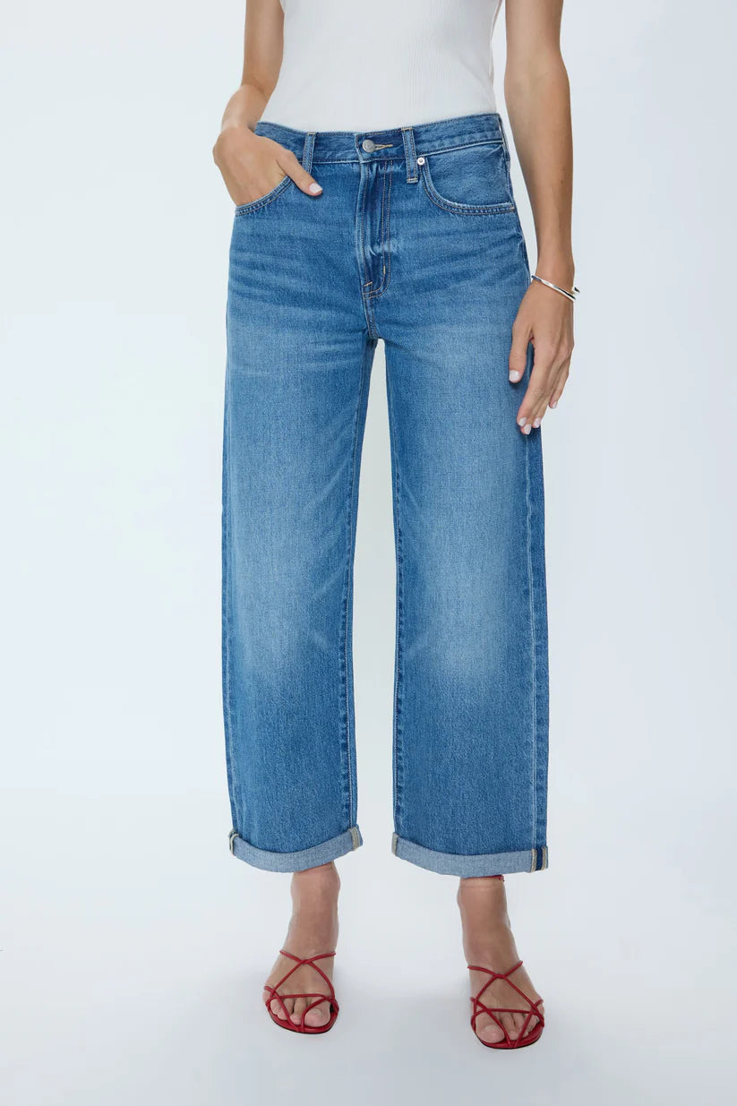 A model wearing a pair of wide-leg cropped blue denim jeans with rolled cuffs, paired with a white top and red strappy heels, shown against a plain white studio background.