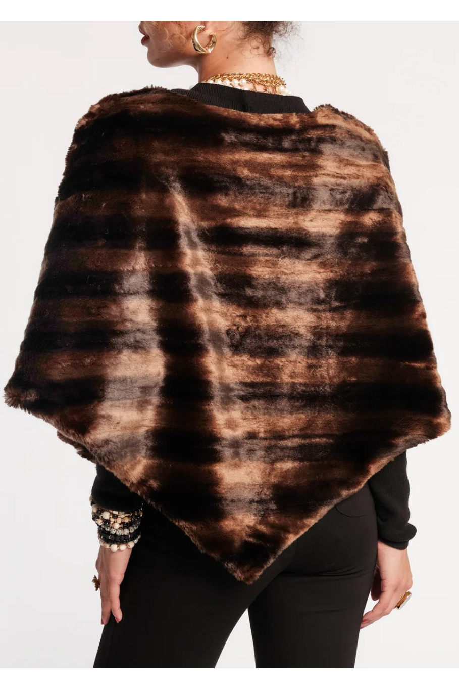 A woman shown from the back wearing a brown and black faux fur poncho over a black top and black pants, against a plain white background.