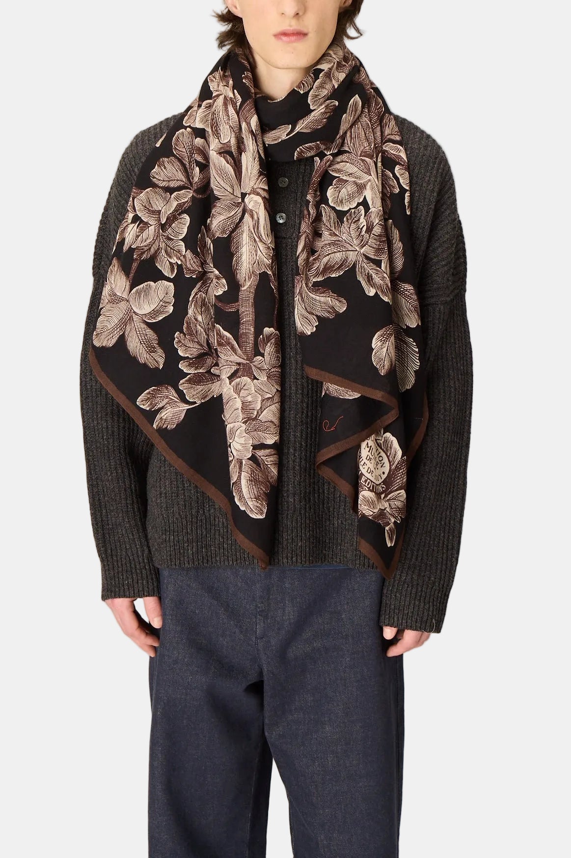 Man wearing a dark sweater and floral-patterned scarf against a plain background