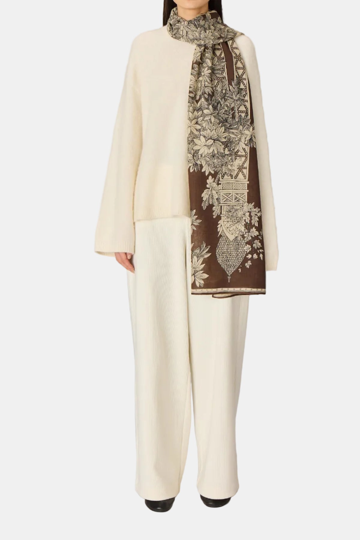 Woman wearing a cream outfit with a patterned scarf against a plain background