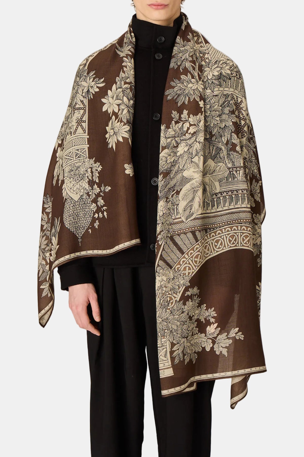 Person wearing a patterned brown scarf on a plain background