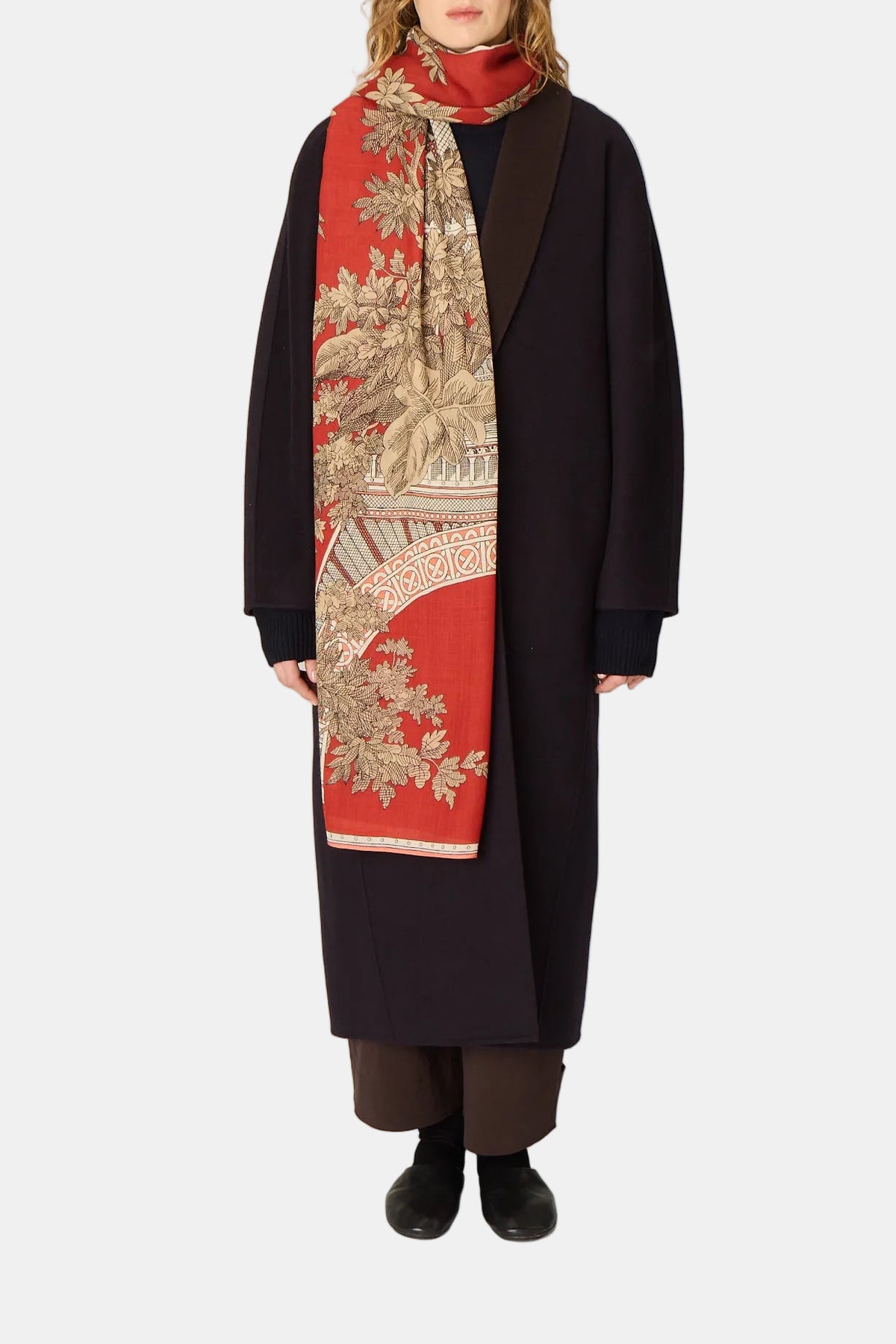 Person wearing a long dark coat and a red patterned scarf on a plain background