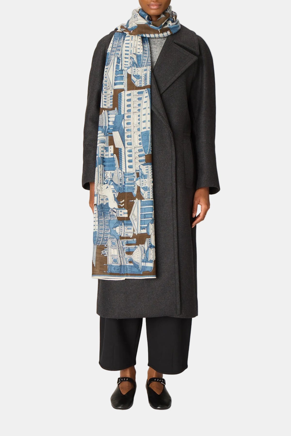 Person wearing a long dark coat and patterned scarf on a plain background