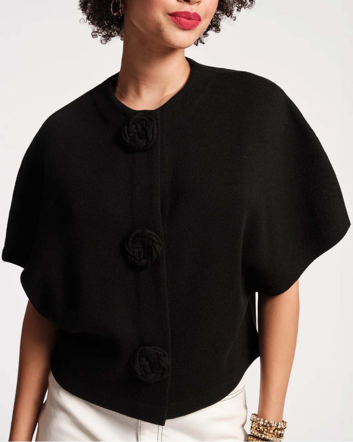 Woman wearing a black poncho with buttons on a light gray background