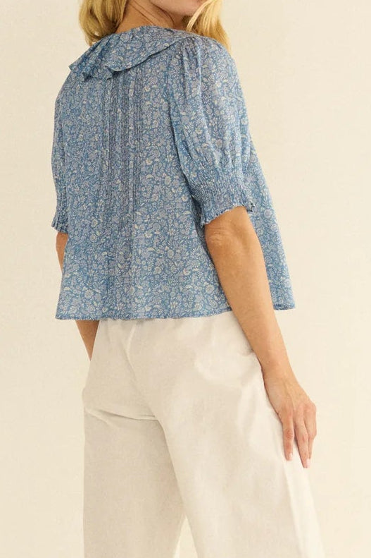 Woman wearing a blue patterned top and white pants on a beige background