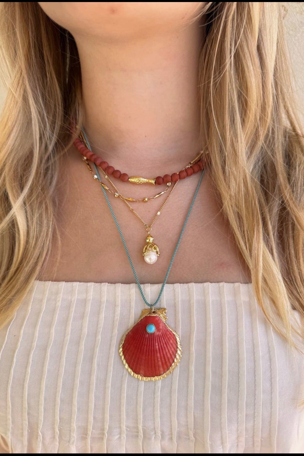 Necklace with shell pendant and other beads on a person wearing a white top.