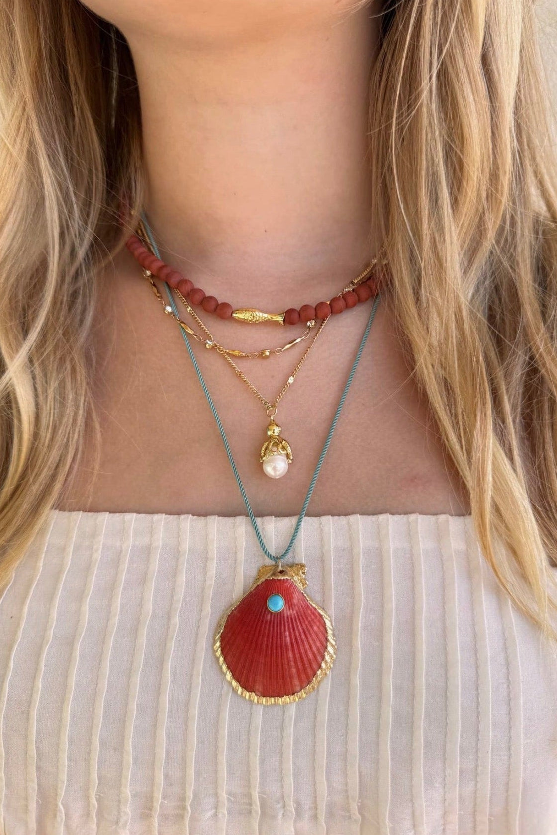 Necklace with shell pendant and other beads on a person wearing a white top.