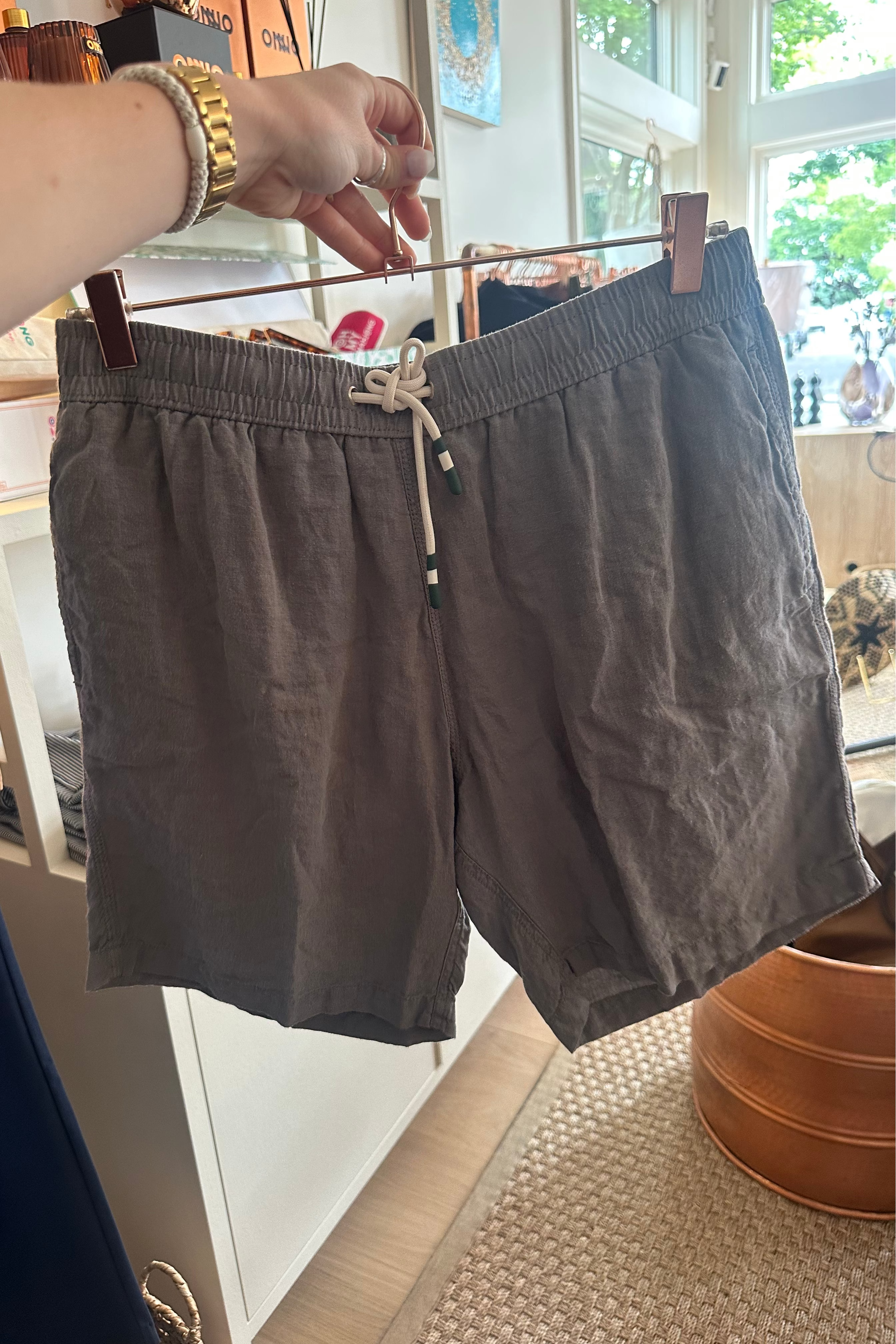 Brown shorts on a hanger in a room with a window and plant.