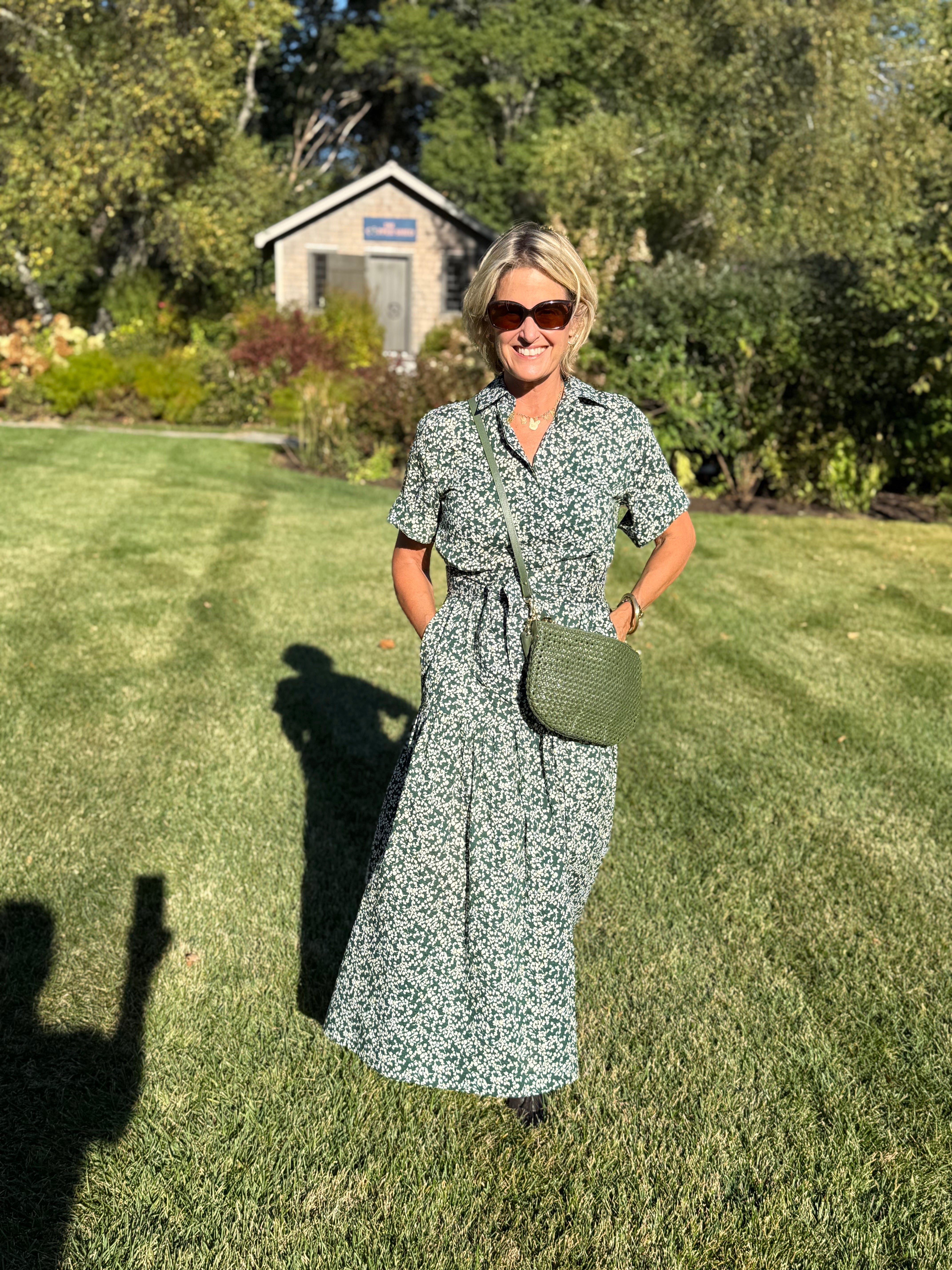 Woman in a green floral dress standing on grass with trees in the background
