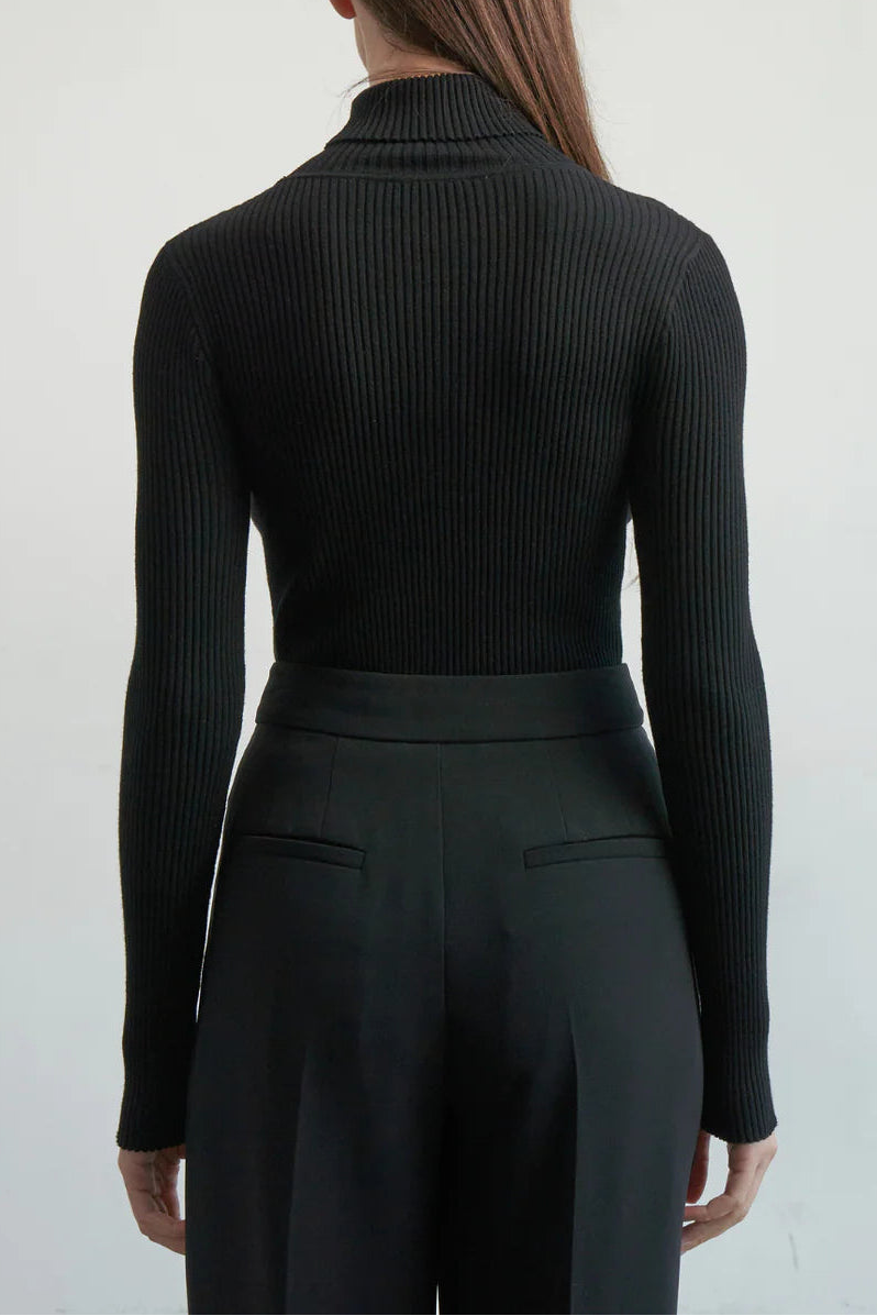Person wearing a black ribbed long-sleeve top and black pants against a white background