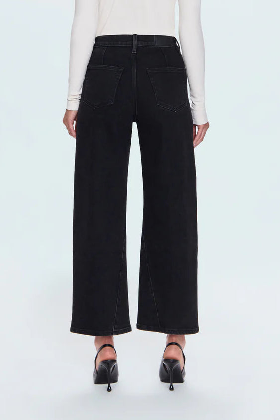 A model viewed from the back wearing a white long-sleeve top, black wide-leg cropped pants, and black heels against a light gray studio background.