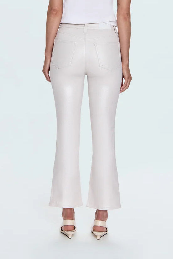 A woman with short blonde hair is shown from the back, wearing a white short-sleeve crop top and light beige flared trousers with metallic gold heels, set against a plain light gray studio background.