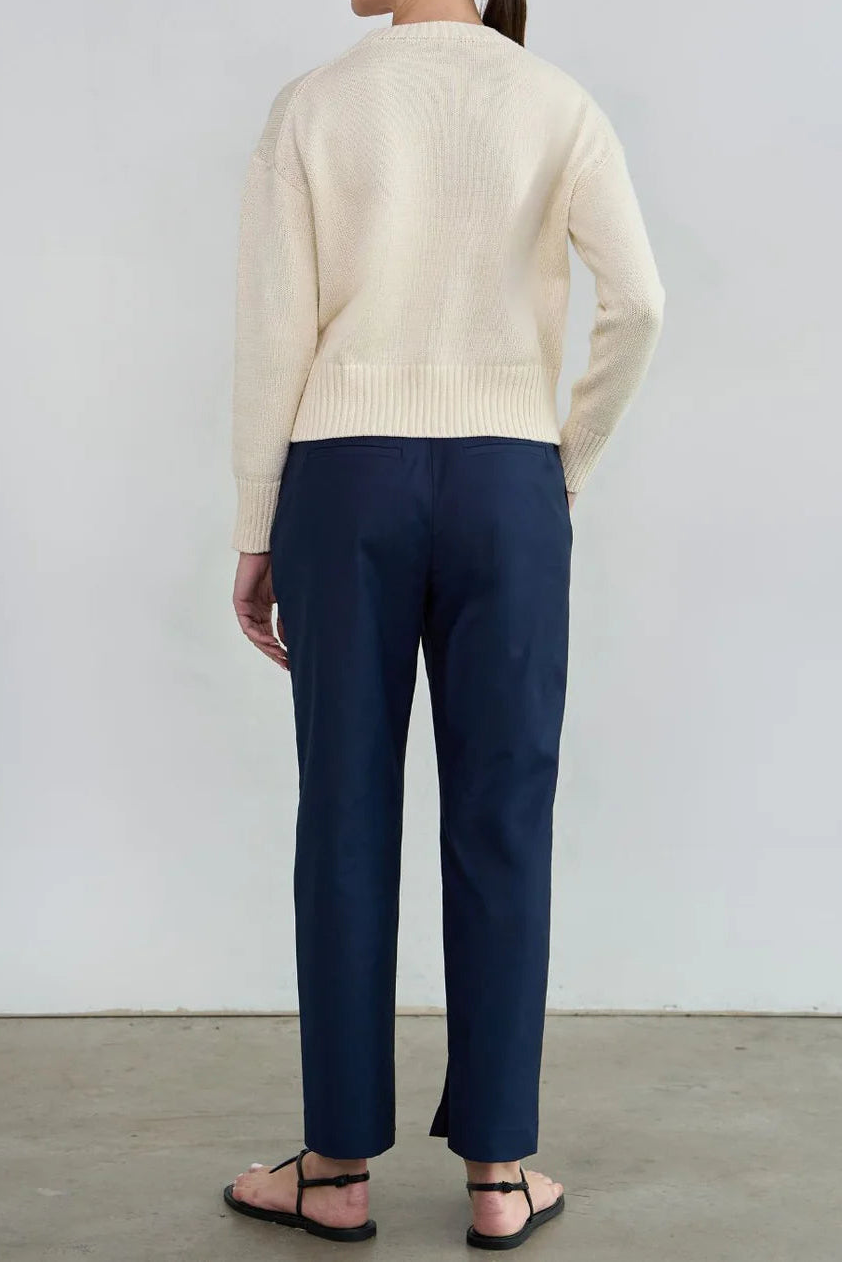 Person wearing a cream sweater and navy pants against a white background