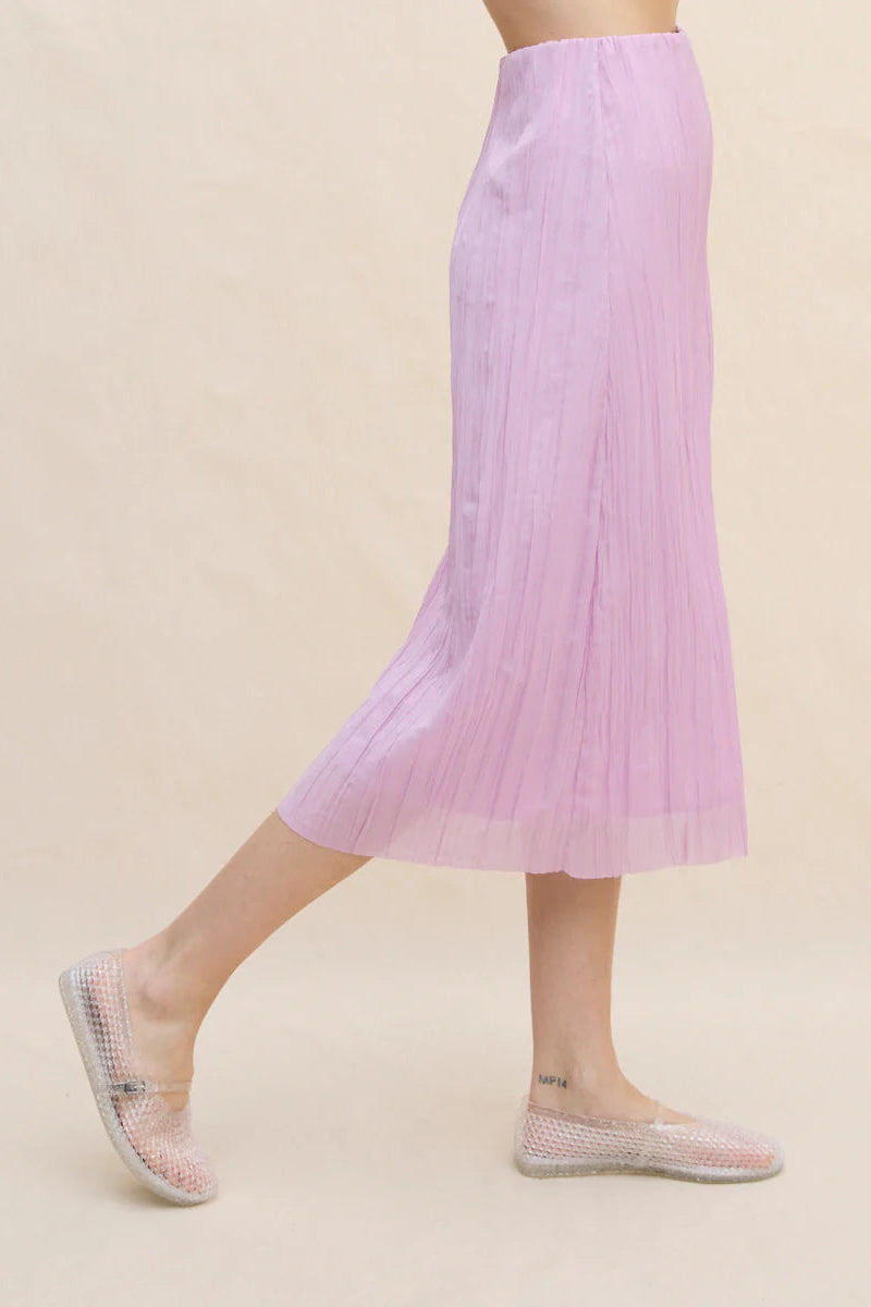 Person wearing a light purple pleated skirt on a beige background
