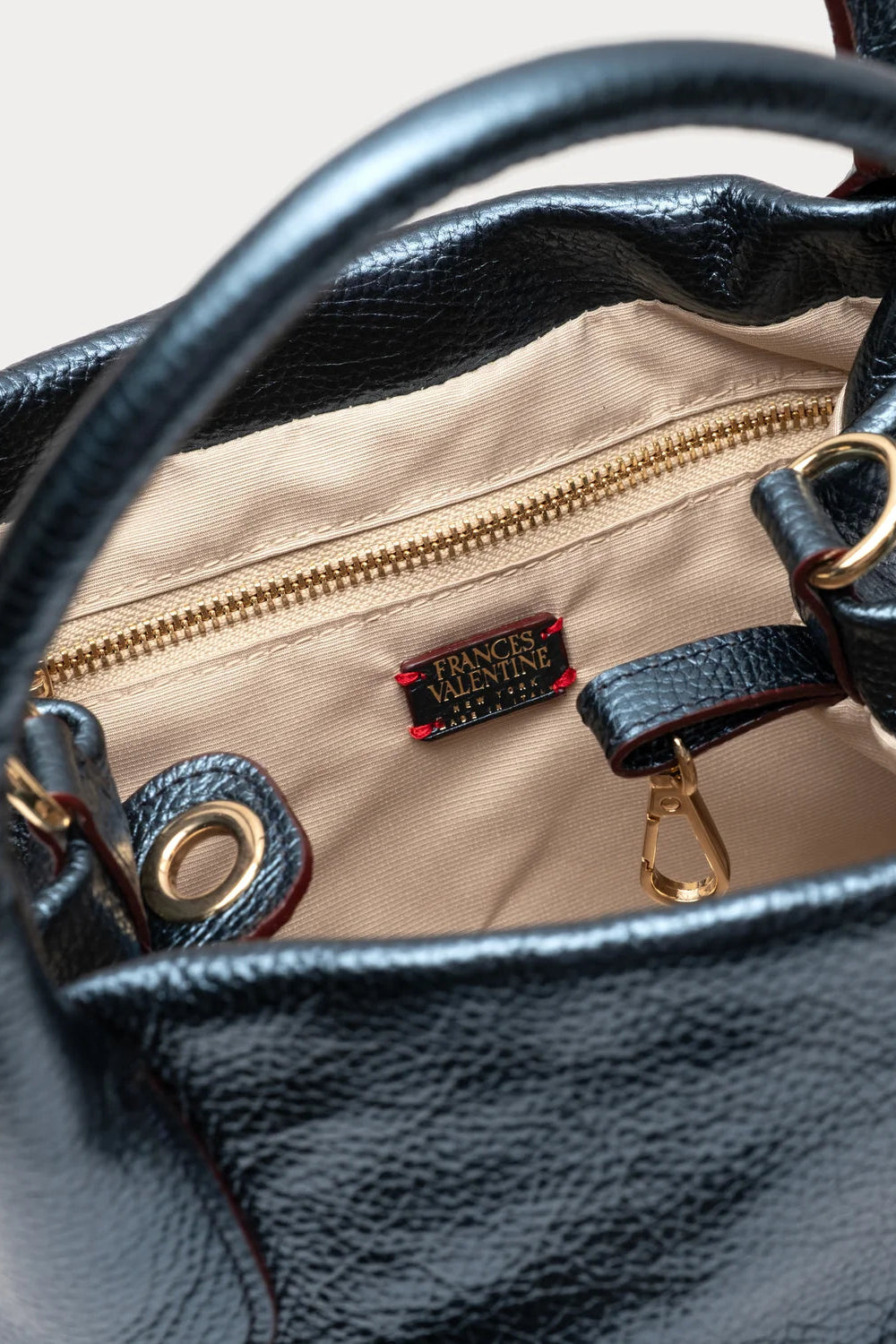 Close-up of the interior of a black pebbled leather handbag, showing a beige nylon lining, gold zipper, and a small black and red brand label that reads Van Cleef & Arpels Paris.