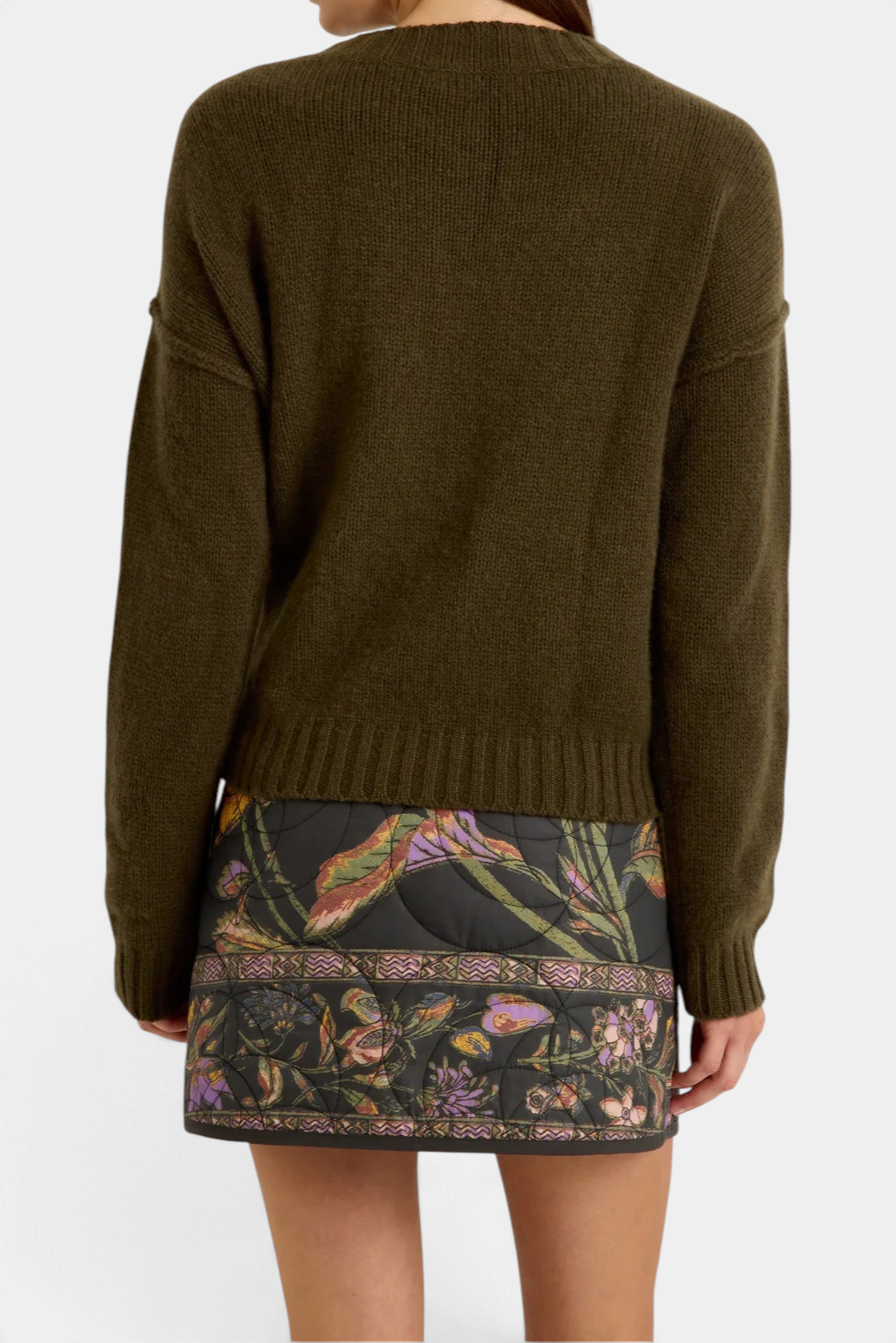 Back view of Marie Oliver Ozzie sweater in olive green cashmere, paired with a floral quilted mini skirt.