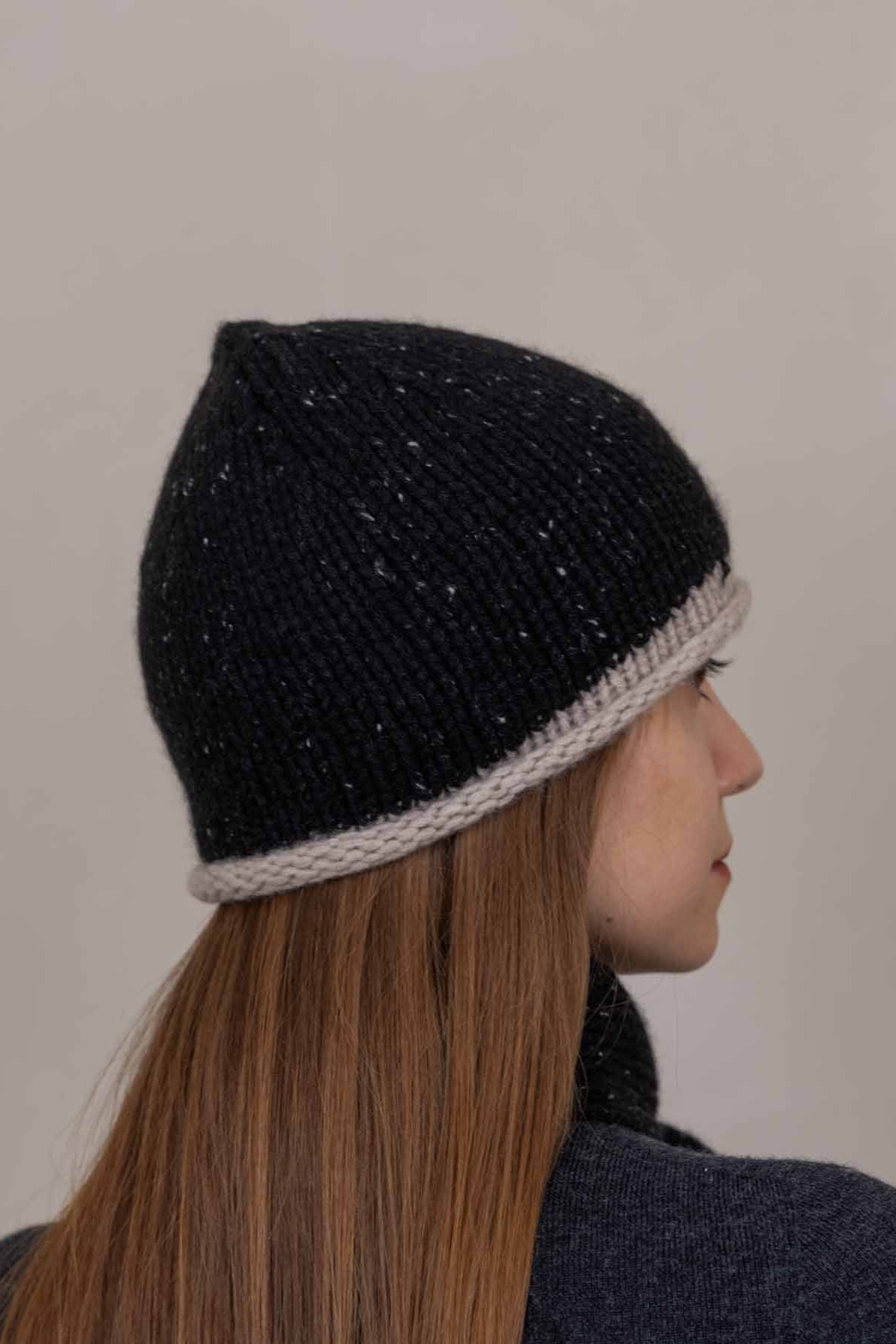 A person shown in side profile wearing a dark navy knit beanie with a light gray ribbed trim, against a plain light gray background.