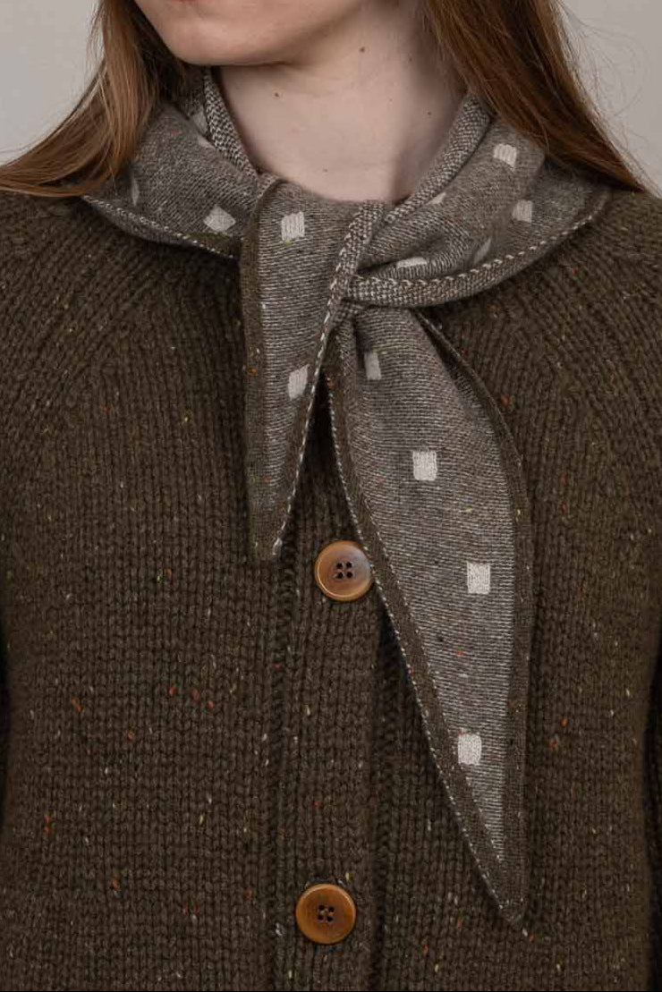 Person wearing a brown coat and hat with a patterned scarf against a plain background