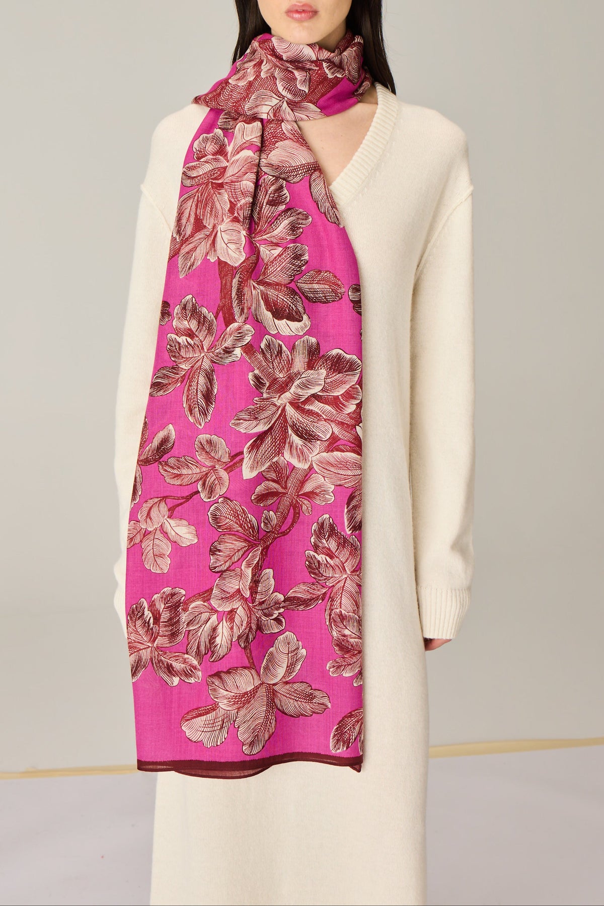 A woman wearing a cream-colored knit sweater and a bright pink scarf with a large floral pattern in dusty rose and brown.