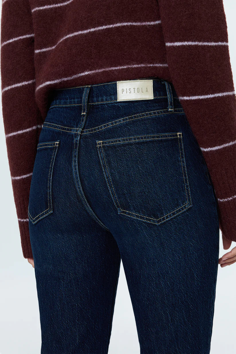 Close-up back view of a person wearing dark blue denim jeans with a visible PISTOLA waistband label and a burgundy striped sweater.