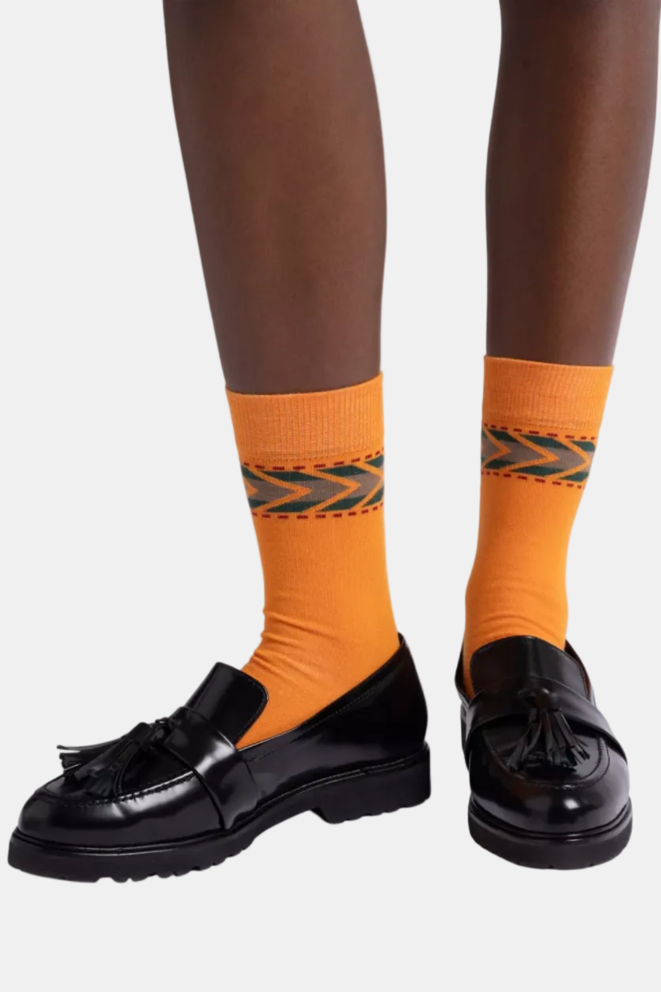 A pair of Irvine tassel leather loafers with a thick tread sole, leather welt detail, and a playful tassel adornment in black color, paired with orange socks.