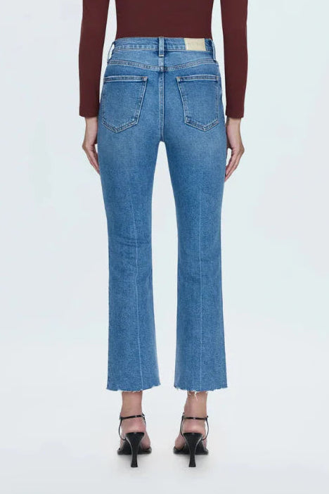 A woman shown from the back wearing a dark burgundy long-sleeve crop top and light blue cropped flare jeans with black high-heeled sandals, against a plain white studio background.