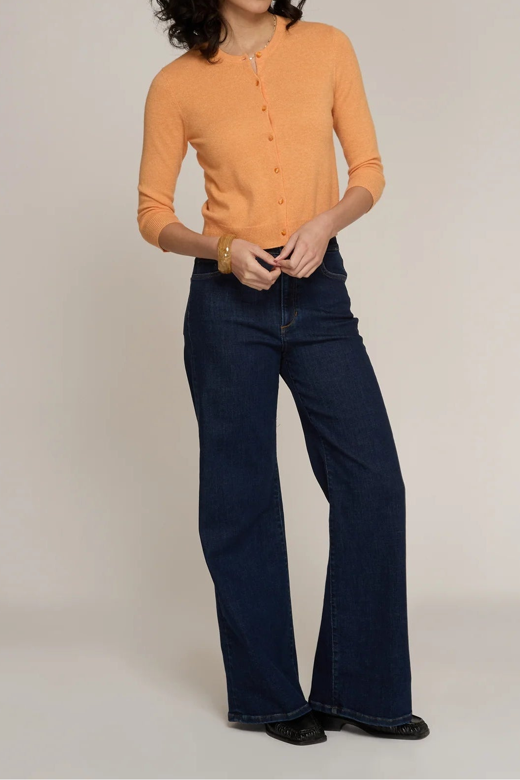 Woman wearing an orange cardigan and dark blue jeans on a plain background
