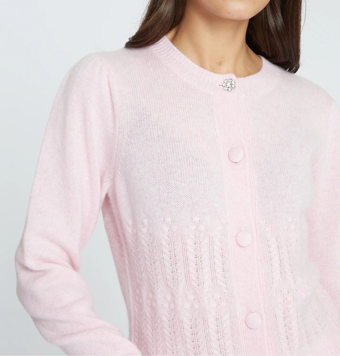 Woman wearing a light pink cardigan against a plain background