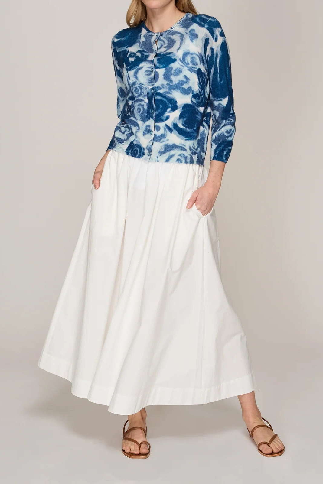 Woman wearing a blue floral top and white skirt on a plain background