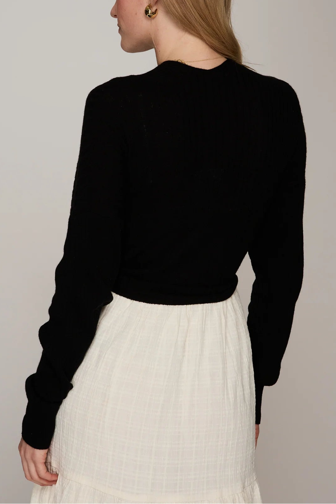 Woman wearing a black long-sleeve top and white pleated skirt on a plain background