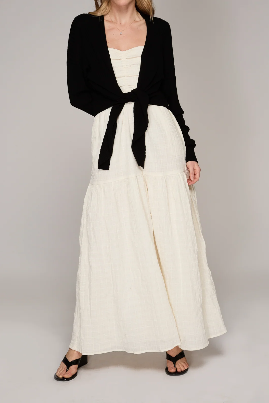 Woman wearing a black cardigan over a white dress on a gray background