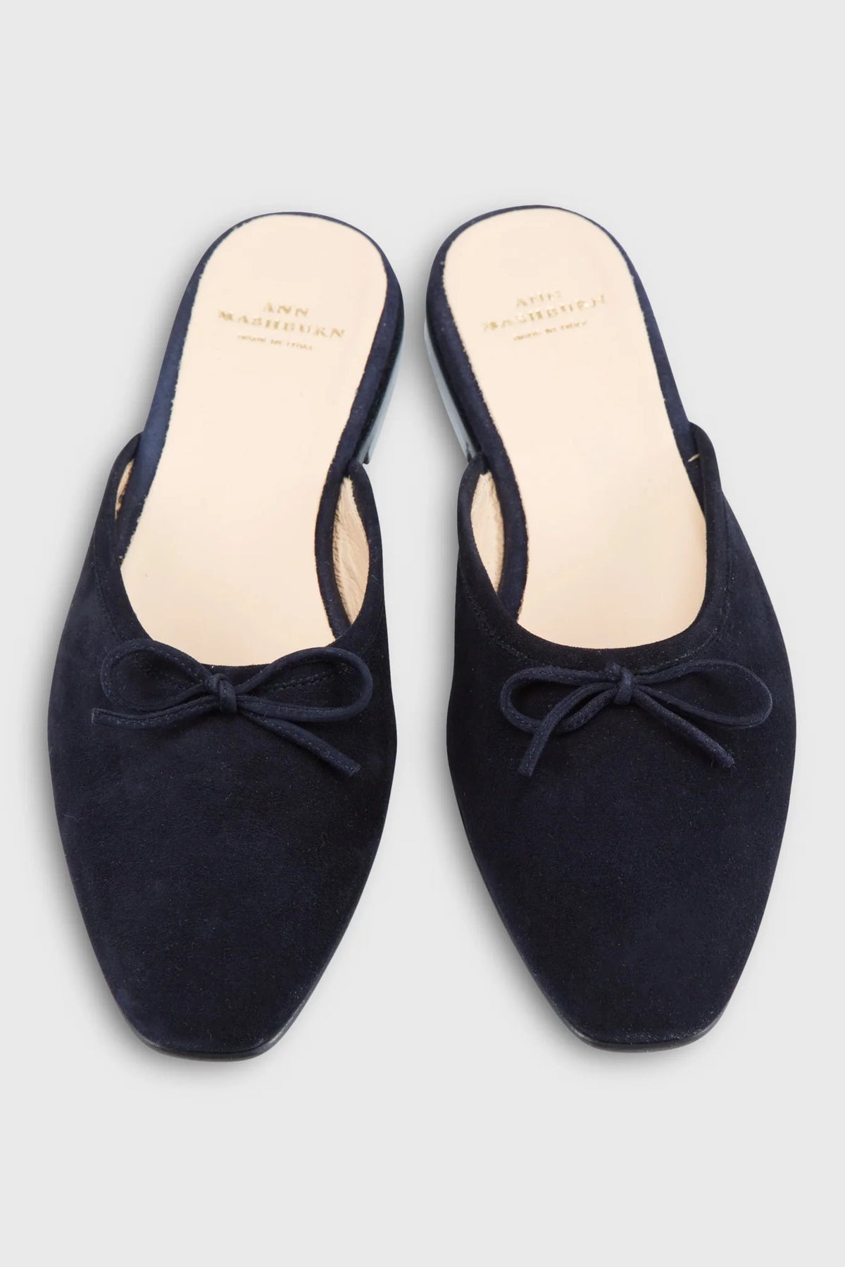 A pair of navy blue suede mule slip-on shoes with a small bow detail on the toe, shown from a top-down view on a light gray background. The brand name 'END MARCHIUTI' is visible on the beige insoles.