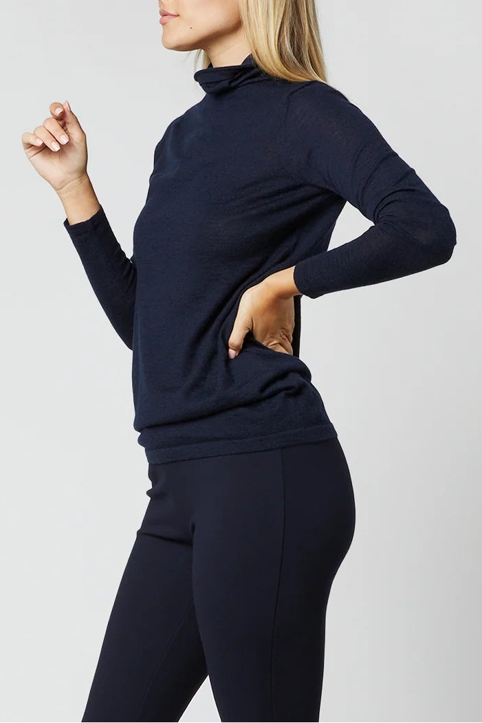 A woman modeling a dark navy blue mock neck long-sleeve top and matching navy blue cropped flare pants, paired with black heels, against a light gray studio background.