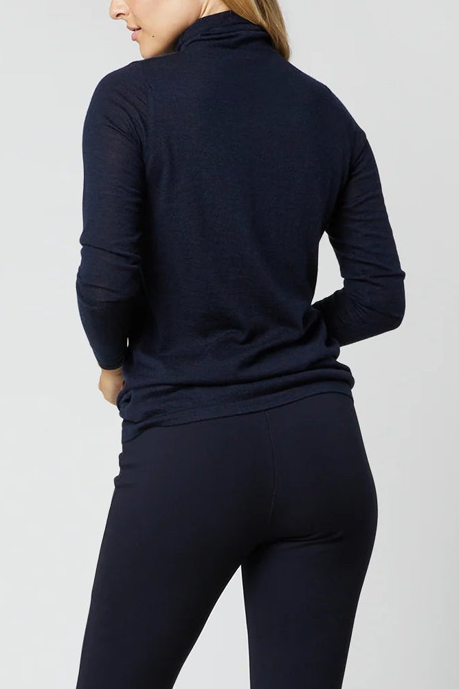 A woman modeling a navy blue mock neck long-sleeve top and matching navy blue flared pants, shown from a rear three-quarter angle against a light gray studio background.