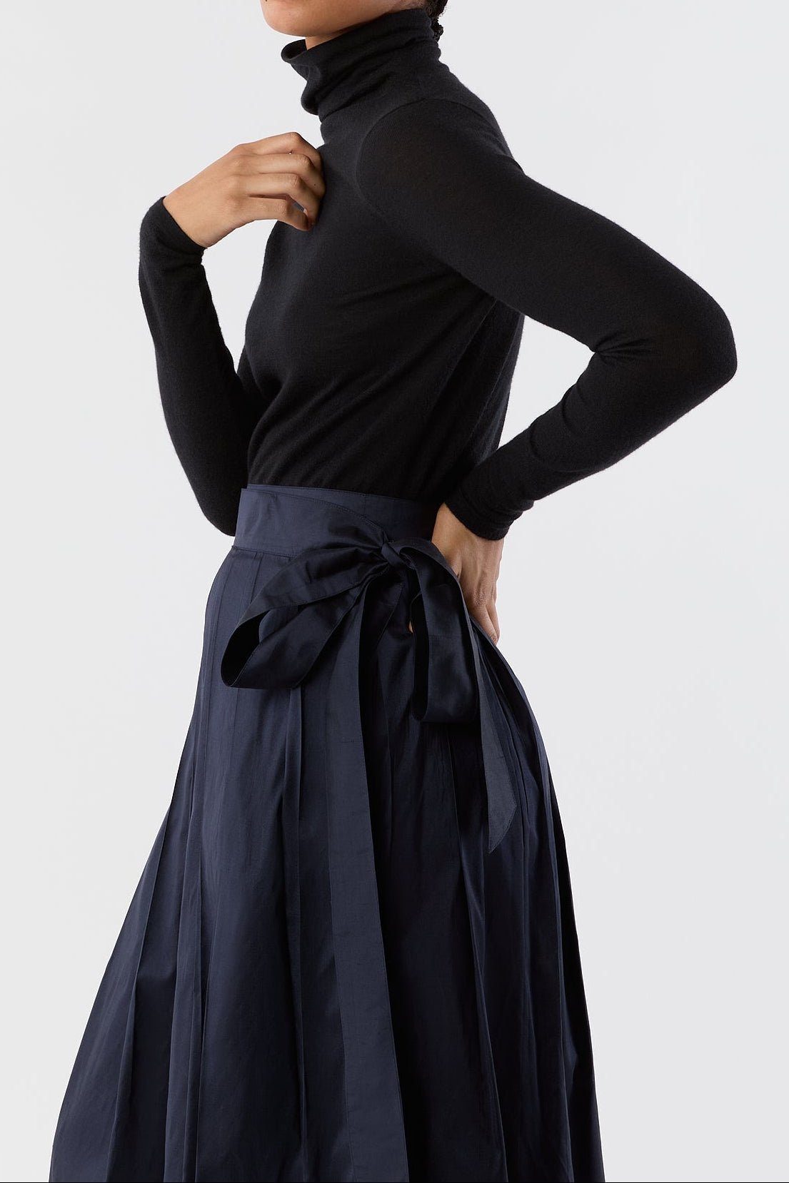 Woman wearing a black turtleneck and navy skirt against a white background