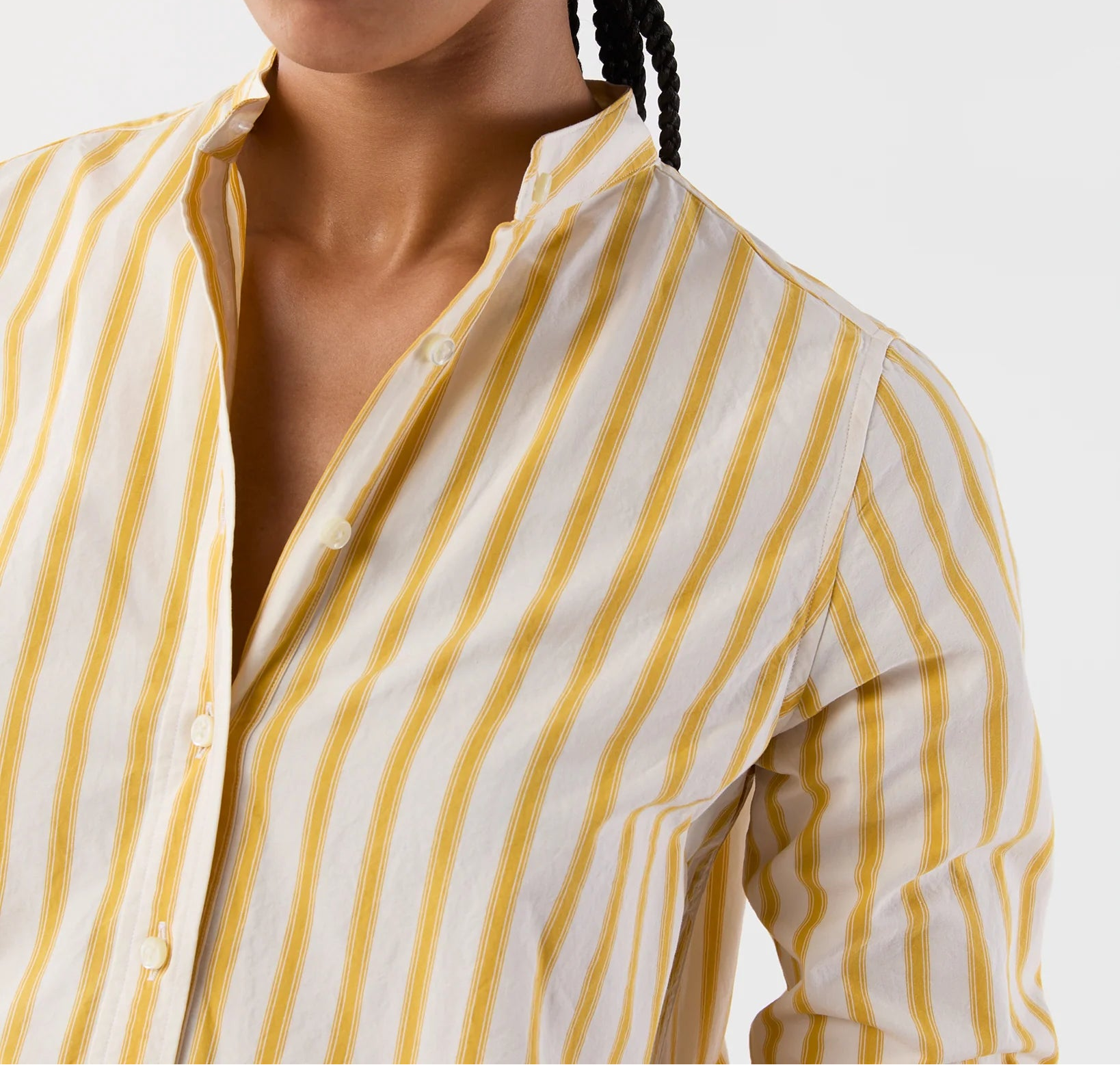 A close-up of a woman wearing a yellow and white vertically striped button-down shirt, cropped from the nose down against a plain light gray background.