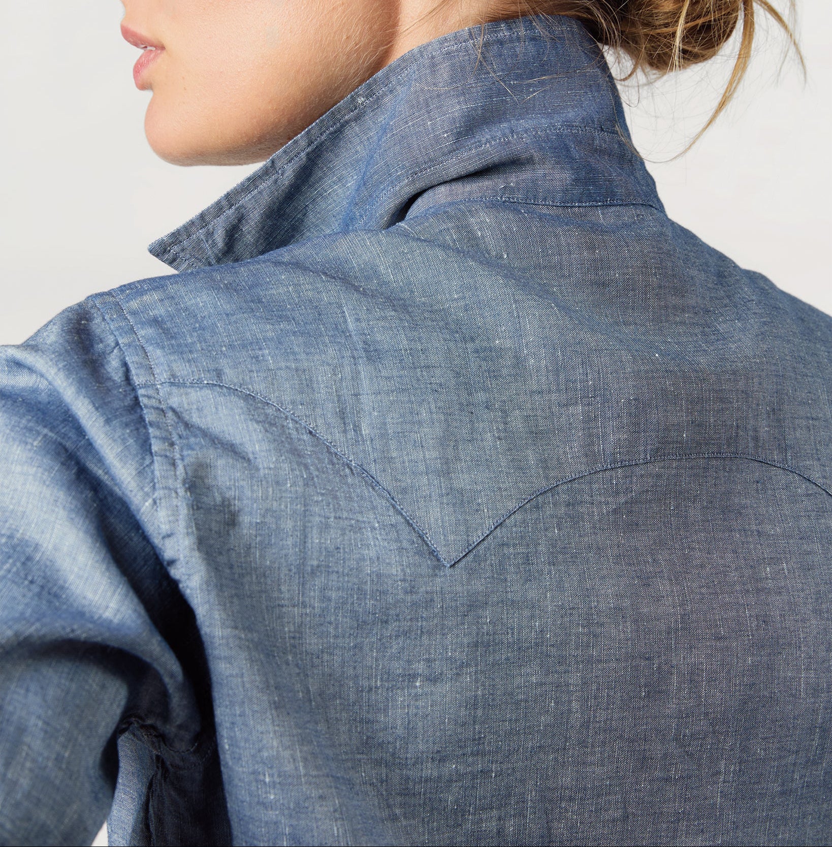 Person wearing a blue denim shirt against a light background