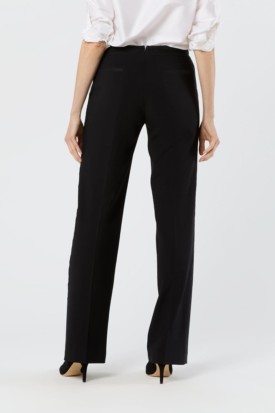 A woman shown from the back wearing a white long-sleeve button-up shirt and black wide-leg trousers, paired with black high heels, against a plain white studio background.