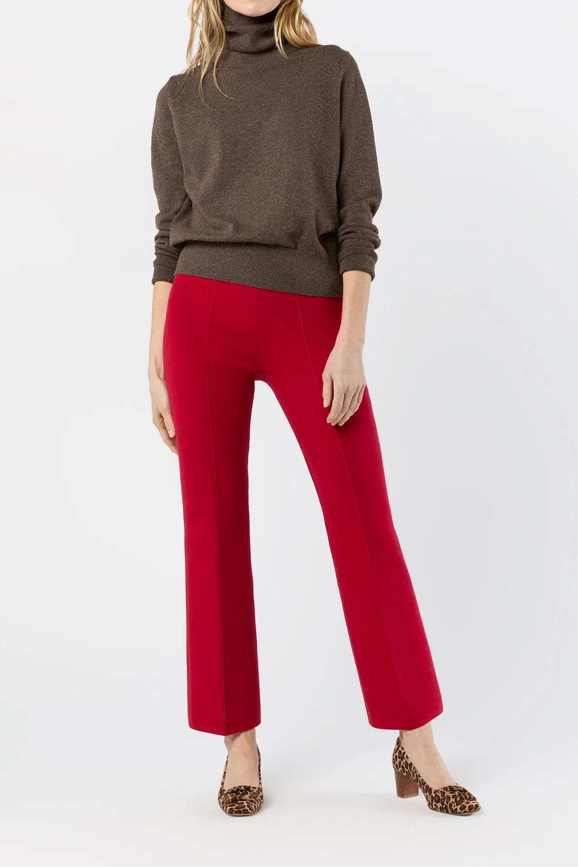 A woman modeling a brown turtleneck sweater and bright red wide-leg cropped pants, paired with leopard-print pointed-toe heels, against a plain white studio background.