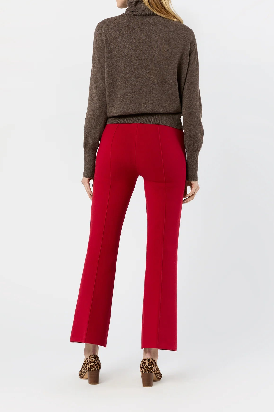 A woman shown from the back wearing a brown cropped turtleneck sweater and bright red cropped flare pants, paired with brown leopard-print heels, against a plain white studio background.