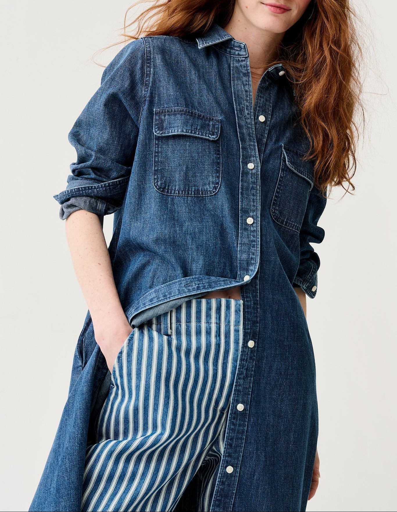 Woman wearing a denim shirt over a striped dress on a plain background
