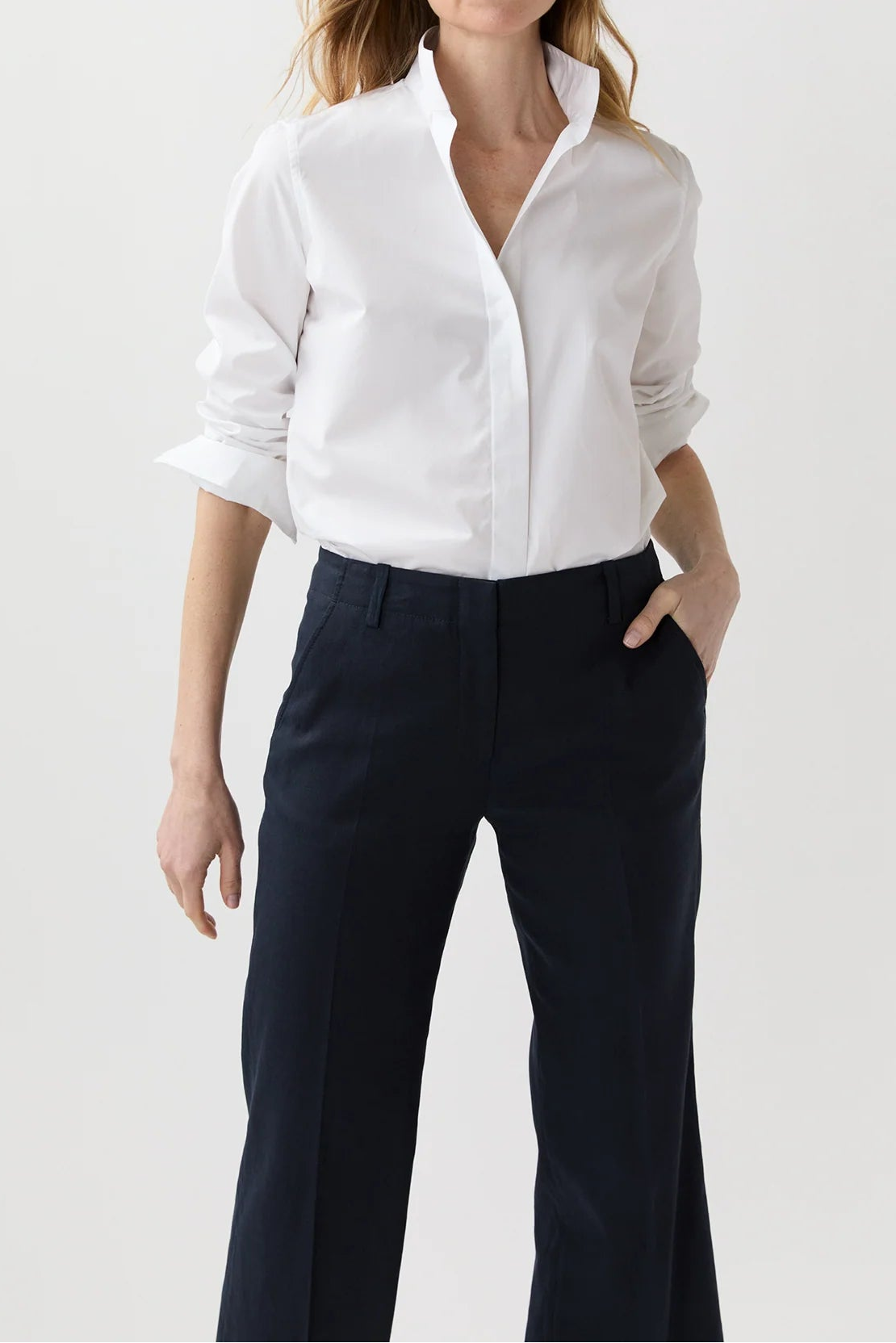 Woman wearing a white shirt and navy pants on a light gray background