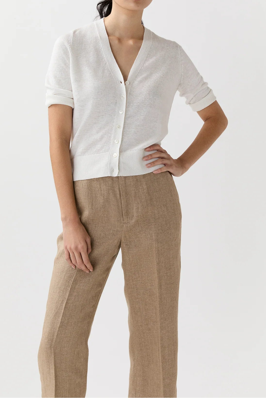 Woman wearing a white blouse and beige pants against a white background