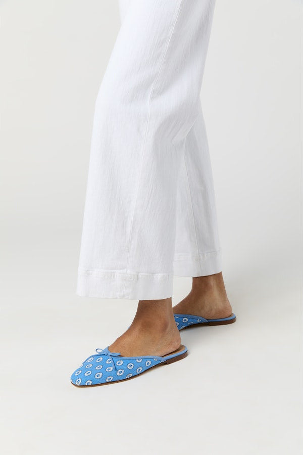 Blue floral slippers worn with white pants on a white background