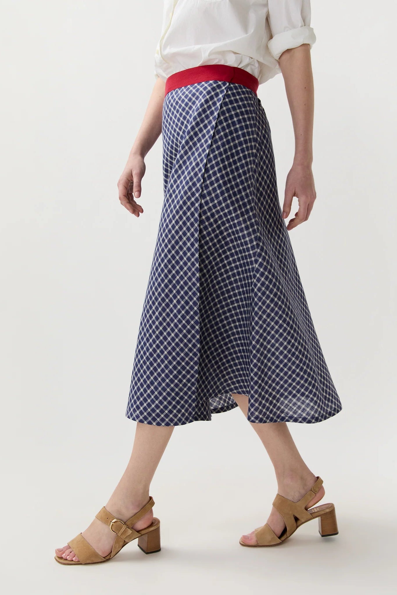 Person wearing a blue plaid skirt with a white top and beige sandals on a light background