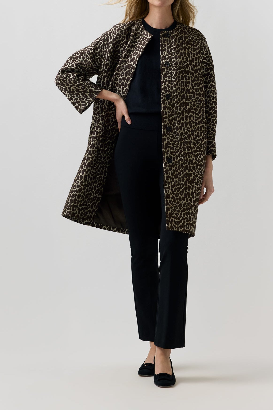 A woman modeling a leopard-print open-front coat over a dark navy outfit, standing against a plain light gray studio background.