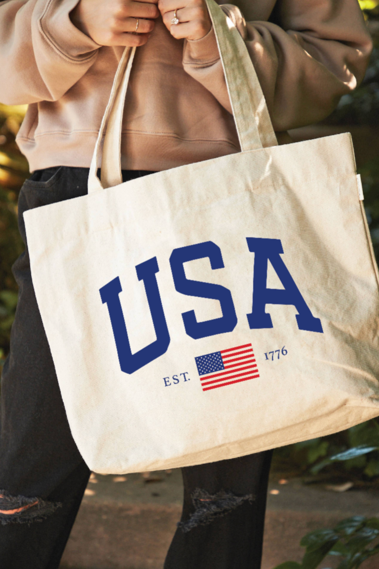 Tote bag with 'USA' and American flag design held by a person outdoors.