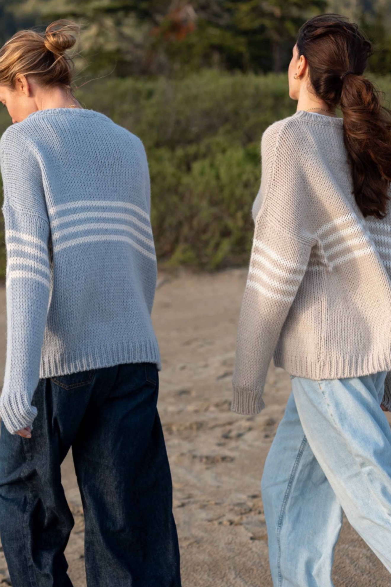 Two people wearing knitted sweaters walking on a beach.